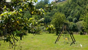 A grassy field with a swing set and a hill with trees in the background.