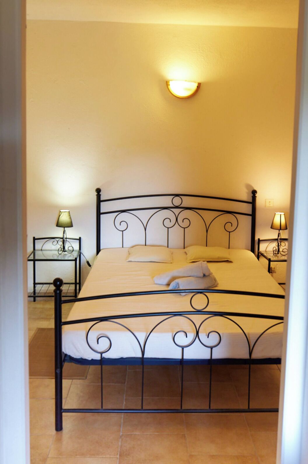 Een bed met een metalen frame, twee nachtkastjes met lampen en een wandlamp.