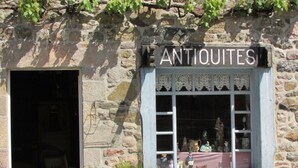 A stone building with a sign reading "ANTIOQUITES" above a window displaying various items. - Sunny family home, 900m. from beach, equipped garden with a shower, WIFI HD, TV (Plurien)
