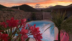 Piscina con muro de piedra y vista a las montañas al atardecer.