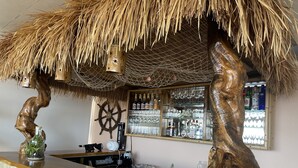 Zona de bar con diseño rústico, que incluye esculturas de madera, una rueda de barco y una variedad de botellas y vasos.