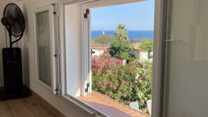 Una habitación con un amplio ventanal corredero que da a un balcón con vistas al mar y al follaje.