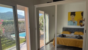 Un dormitorio con una cama, un cuadro y vistas a una piscina y montañas.