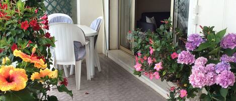 A balcony with a table and chairs, surrounded by potted plants with flowers.