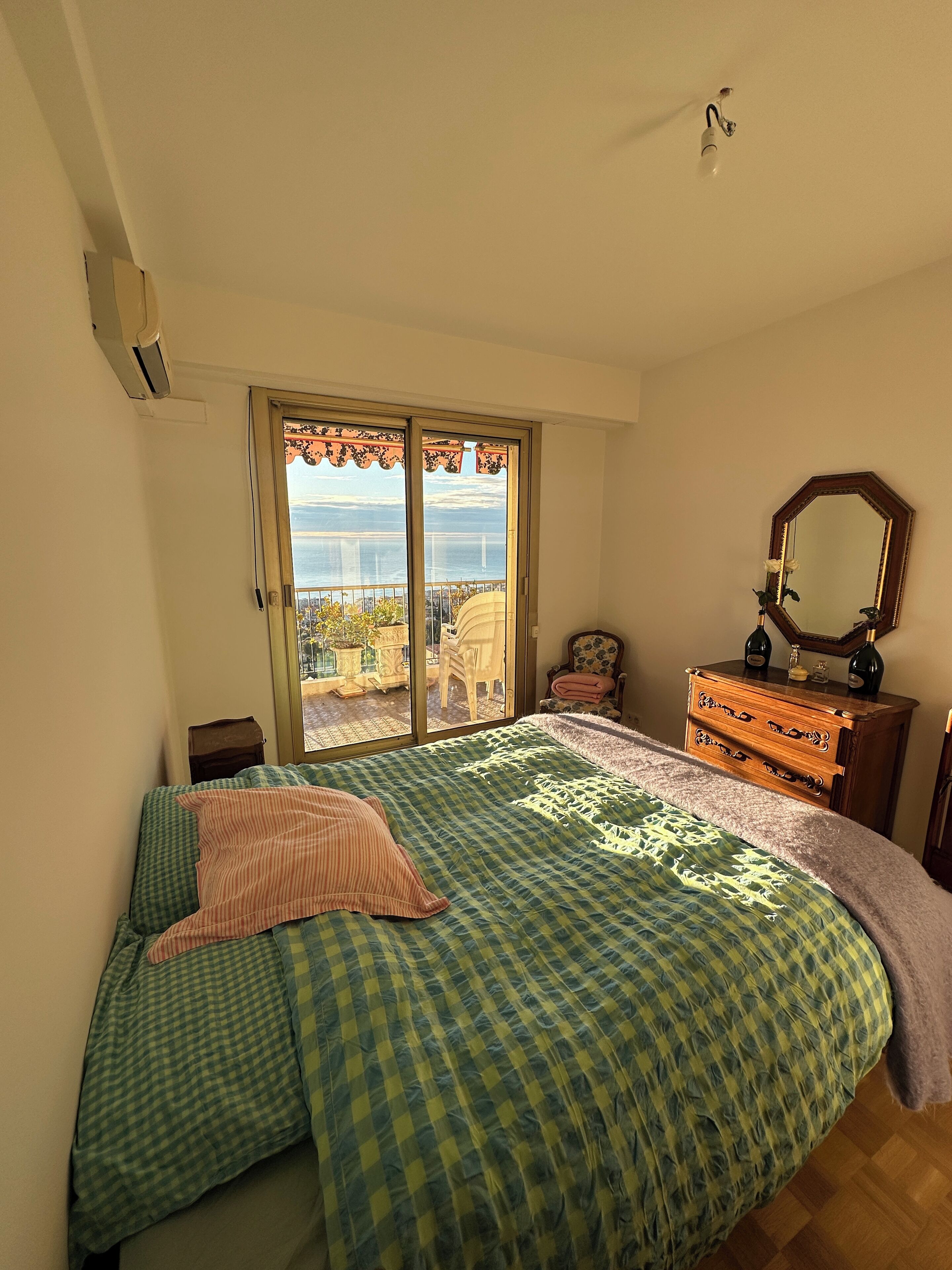 Ein Schlafzimmer mit einem großen Bett, einem Schminktisch, einem Spiegel und Meerblick durch eine Schiebetür.