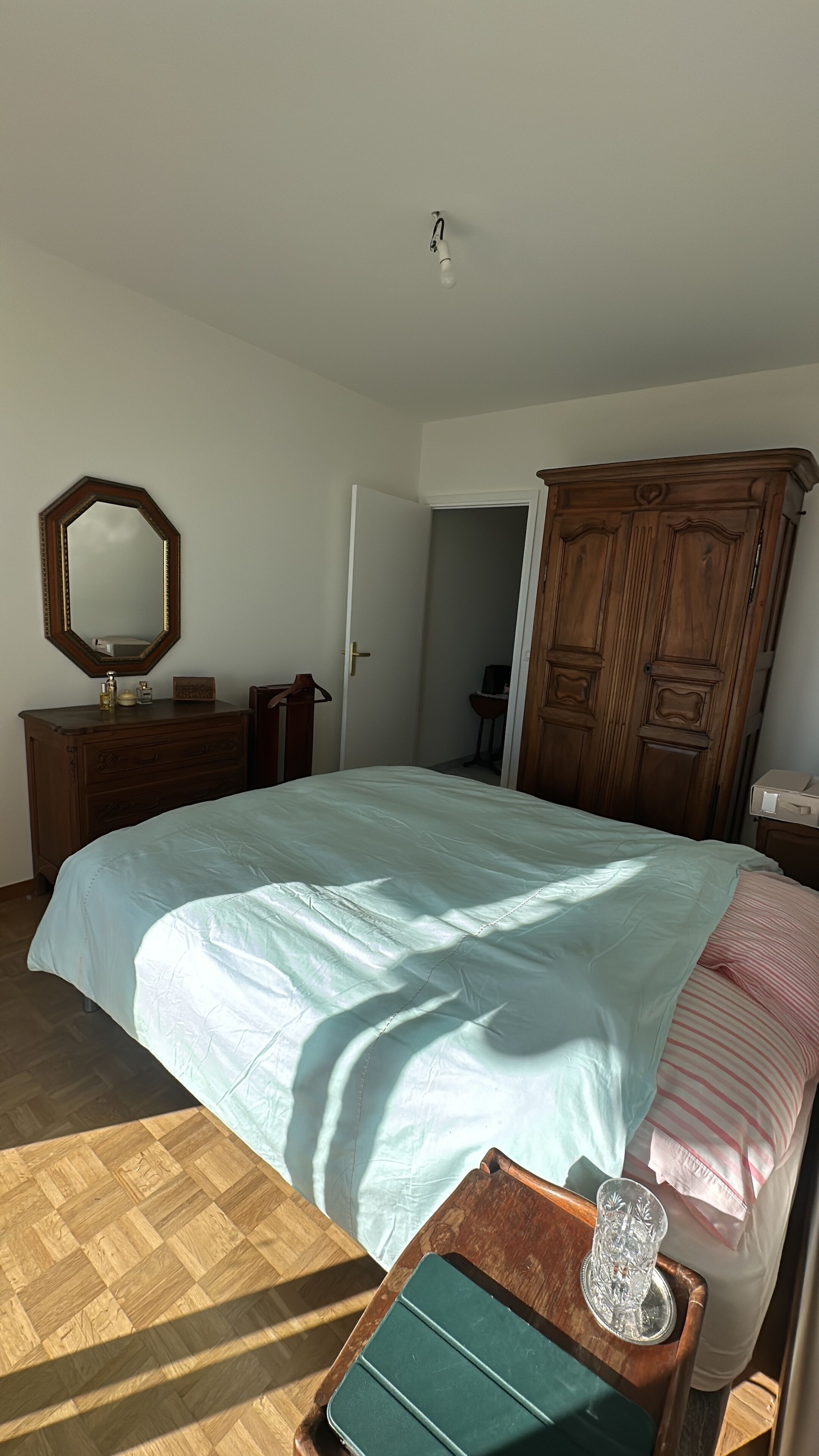 Une chambre à coucher avec un grand lit, une armoire en bois, une commode et une petite table avec un verre.