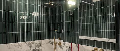 A modern bathroom with a freestanding bathtub, a large mirror, and dark green tiled walls.