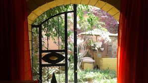Un arco de entrada con una reja metálica que da a un jardín con plantas y un muro de piedra.
