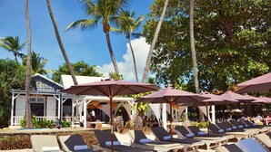 Un resort frente a la playa con sillones de descanso y sombrillas, una piscina y palmeras.