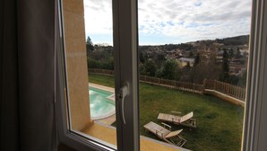 A view from a balcony overlooking a swimming pool, a grassy area with lounge chairs, and a distant townscape.