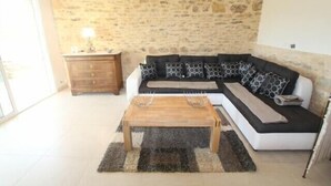A living room with a stone wall, a sofa with patterned cushions, a wooden coffee table, and a small wooden cabinet.
