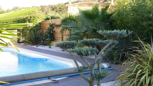 A swimming pool surrounded by gravel, with a wooden fence and various plants. - Very beautiful wooded villa, heated swimming pool, breathtaking view - 8/10 people (Les Cluses)