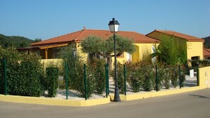 A yellow building with a red-tiled roof, surrounded by greenery and a street lamp. - Very beautiful wooded villa, heated swimming pool, breathtaking view - 8/10 people (Les Cluses)