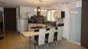 A compact kitchen with a central island, a refrigerator, microwave, and a sink. There are four chairs around the island. - Very beautiful wooded villa, heated swimming pool, breathtaking view - 8/10 people (Les Cluses)