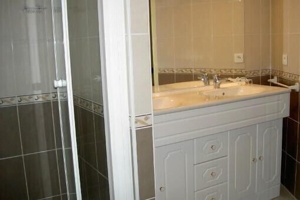 A bathroom with a shower, a sink with a mirror, and a cabinet with drawers. - Panoramic view of the port of Camaret sur Mer (Camaret-Sur-Mer)