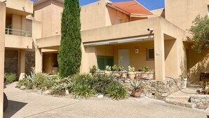 Un bâtiment moderne doté d’un toit plat, d’un grand conifère et de plantes en pot dans la cour.