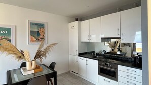 Une cuisine moderne avec des meubles blancs, un plan de travail noir et un coin repas comprenant une table et des chaises en verre.