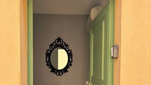 Un couloir avec une porte verte, un meuble noir et un miroir au mur.