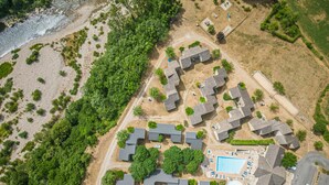 An aerial view of a residential area with multiple houses, a swimming pool, and a beach. - Logement 4/6 pers. - Blajoux (Quézac)