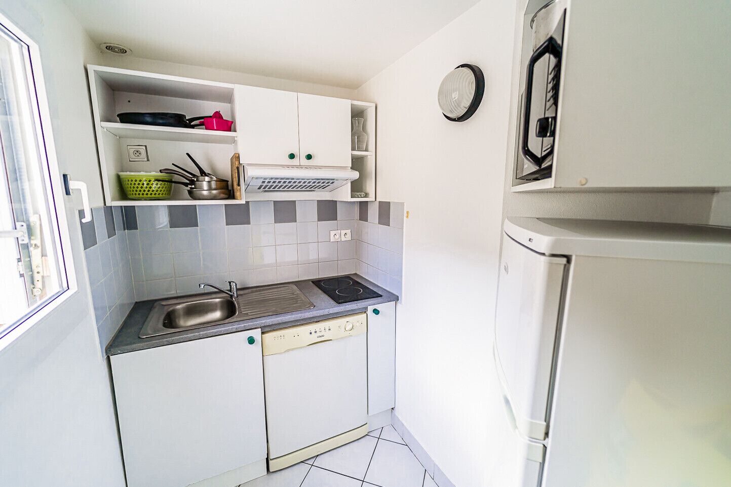 A compact kitchen with a sink, stove, and dishwasher. There is a refrigerator and a window on the left side.