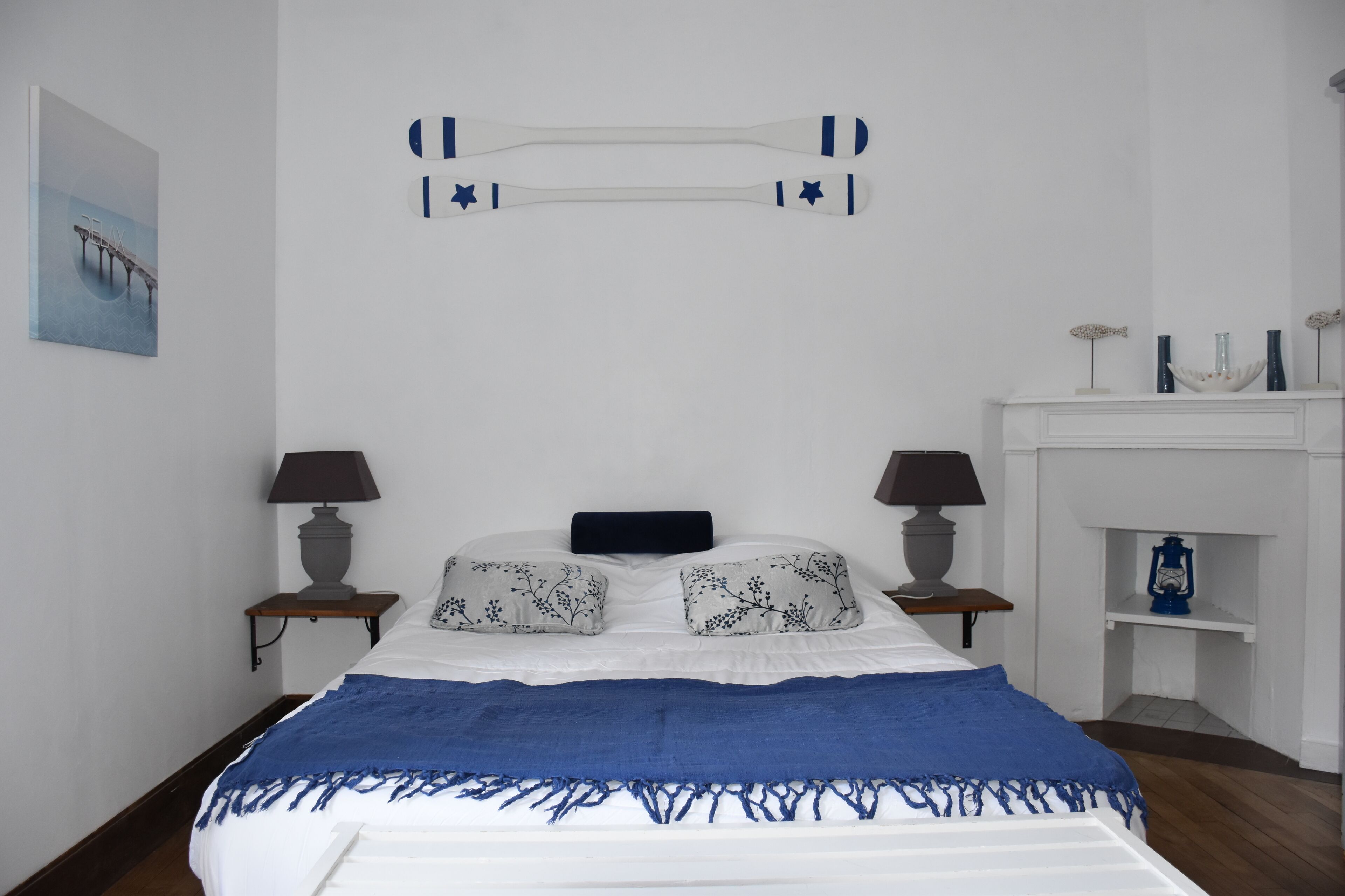 A bedroom with a bed, two bedside tables with lamps, a fireplace, and a wall-mounted decoration.