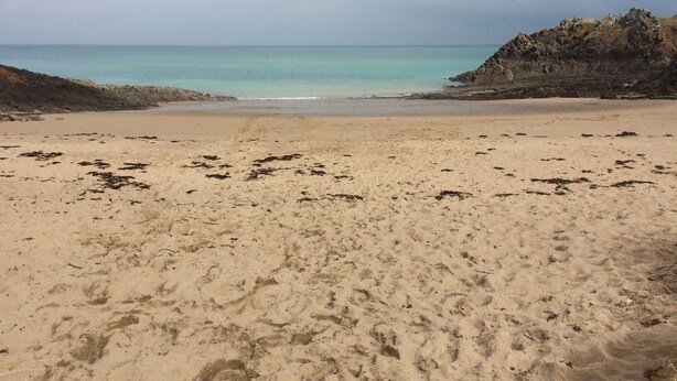 Une plage avec un promontoire rocheux sur la droite et une mer calme.