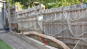 Une clôture en bois avec un enclos grillagé et un pont en rondin qui enjambe un chemin de gravier.