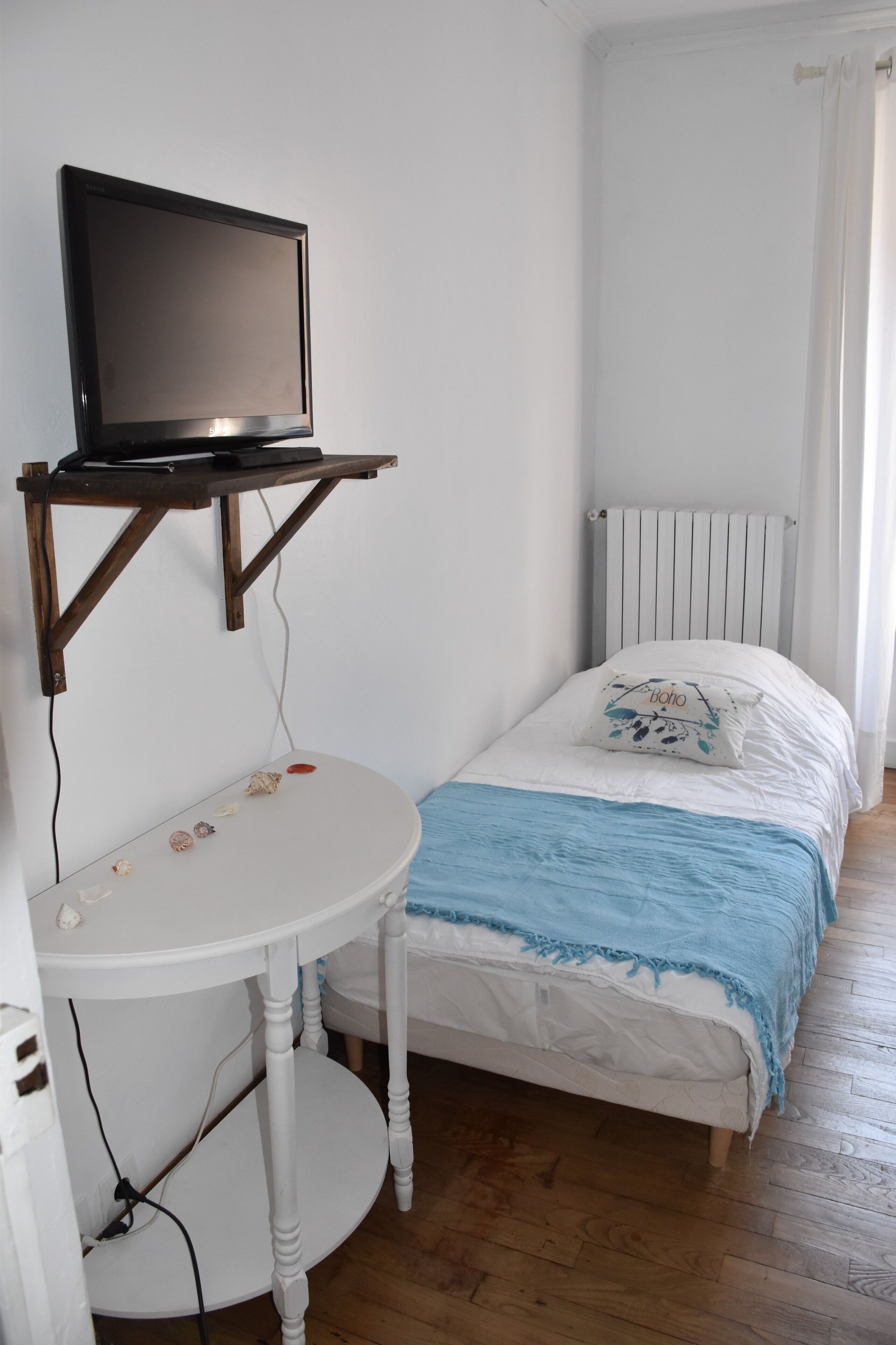 Ein kleiner, ordentlicher Raum mit einem Bett, einem weißen Tisch und einem Fernseher darauf sowie einer Heizung.