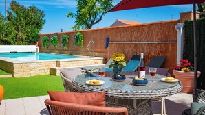 Un patio exterior con piscina, muebles de mimbre y una mesa dispuesta con comida y bebidas.
