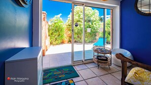 Una habitación con un gran ventanal corredera que da a un jardín, una silla de mimbre, un sofá blanco y una pared azul.