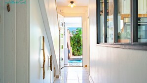 Un pasillo con suelo de baldosas que conduce a una puerta con vistas a un jardín y una piscina.