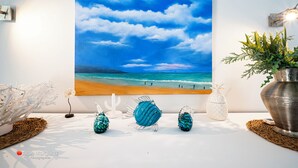 Pintura de una escena de playa en una pared, peces de vidrio decorativos y una planta en maceta.