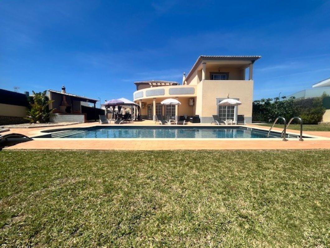 A modern house with a swimming pool, outdoor seating, and a well-maintained lawn.