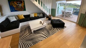 A modern living room with a black and white patterned rug, a white coffee table, a black sofa with yellow cushions, and a staircase leading to a balcony with outdoor furniture.