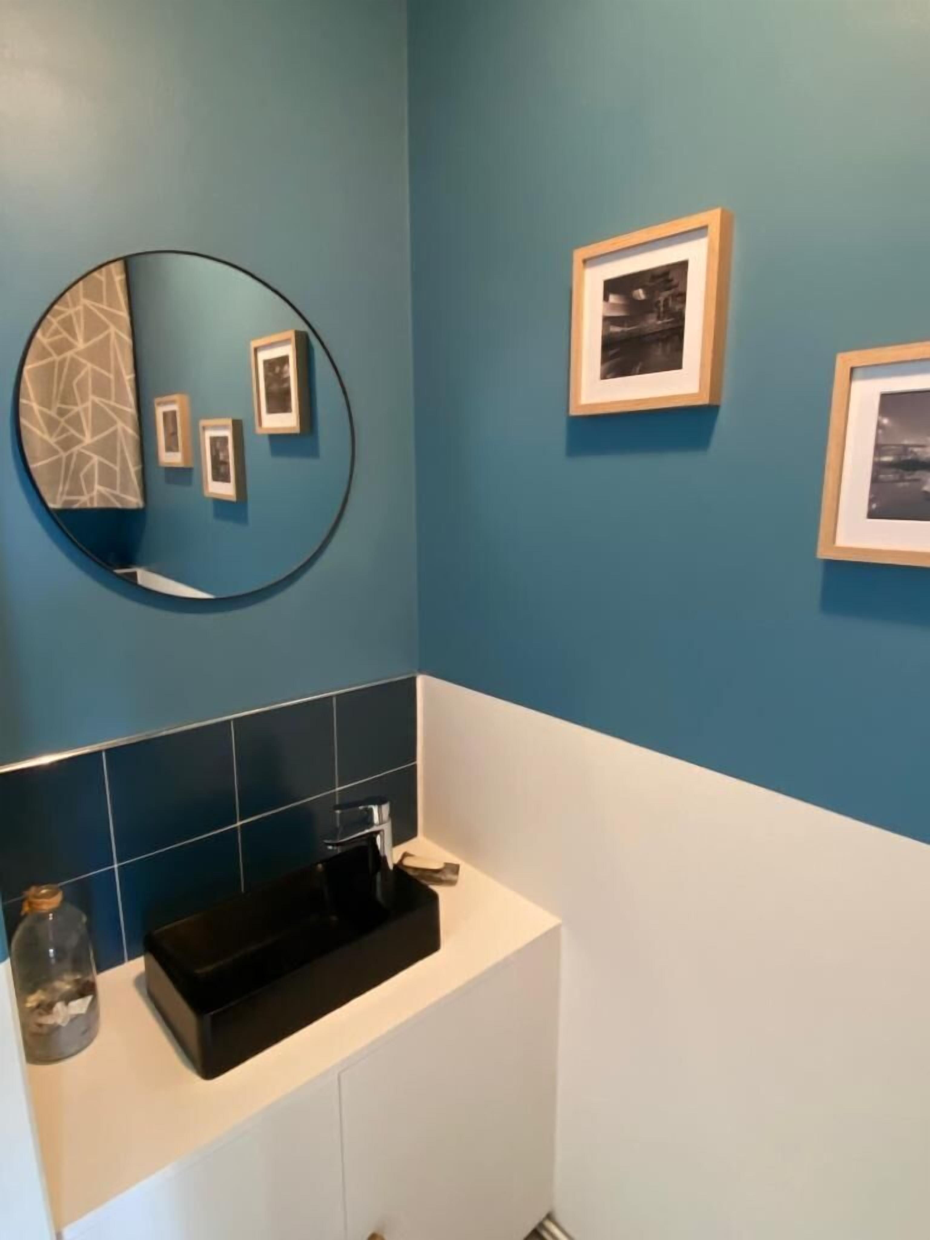 A bathroom with a blue wall, a round mirror, a black sink, and three framed pictures.