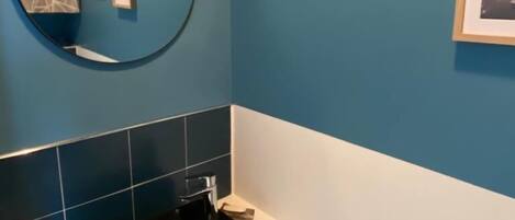 A bathroom with a blue wall, a round mirror, a black sink, and three framed pictures.