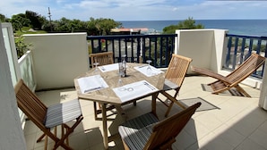 A balcony with a wooden table and chairs, a view of the sea, and a blue railing.