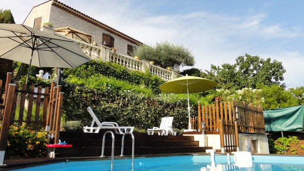 Una piscina con sillas de descanso y sombrillas, rodeada por una valla de madera y follaje.