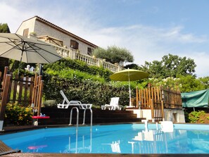 Ein Pool mit Liegestühlen und Sonnenschirmen, umgeben von einem Holzzaun und viel Grün.