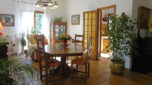 Comedor con una mesa y sillas de madera, rodeado de plantas en macetas y una lámpara de araña.