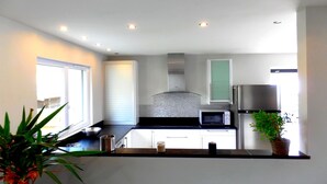 A modern kitchen with white cabinets, a stainless steel range hood, a microwave, and a refrigerator.