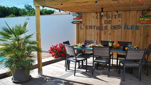 An outdoor dining area with a wooden pergola, a table set for two, and a potted plant.