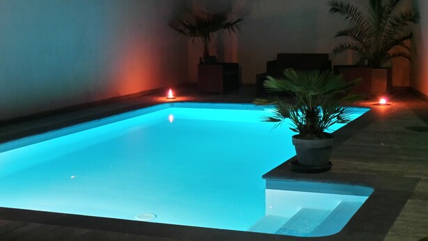 A swimming pool with a blue illuminated edge, surrounded by walls and potted plants.