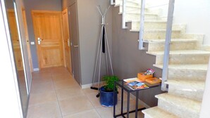 A hallway with a wooden door, a metal staircase, and a small table with magazines and a plant.