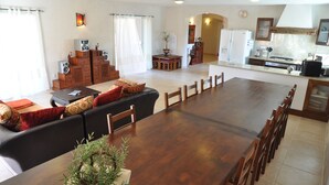 Ein geräumiges Wohnzimmer mit einem großen Esstisch aus Holz, einer schwarzen Couch mit roten Kissen und einem kleinen Holzschrank.