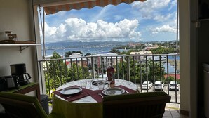A balcony with a table set for two, overlooking a coastal town with boats and buildings.