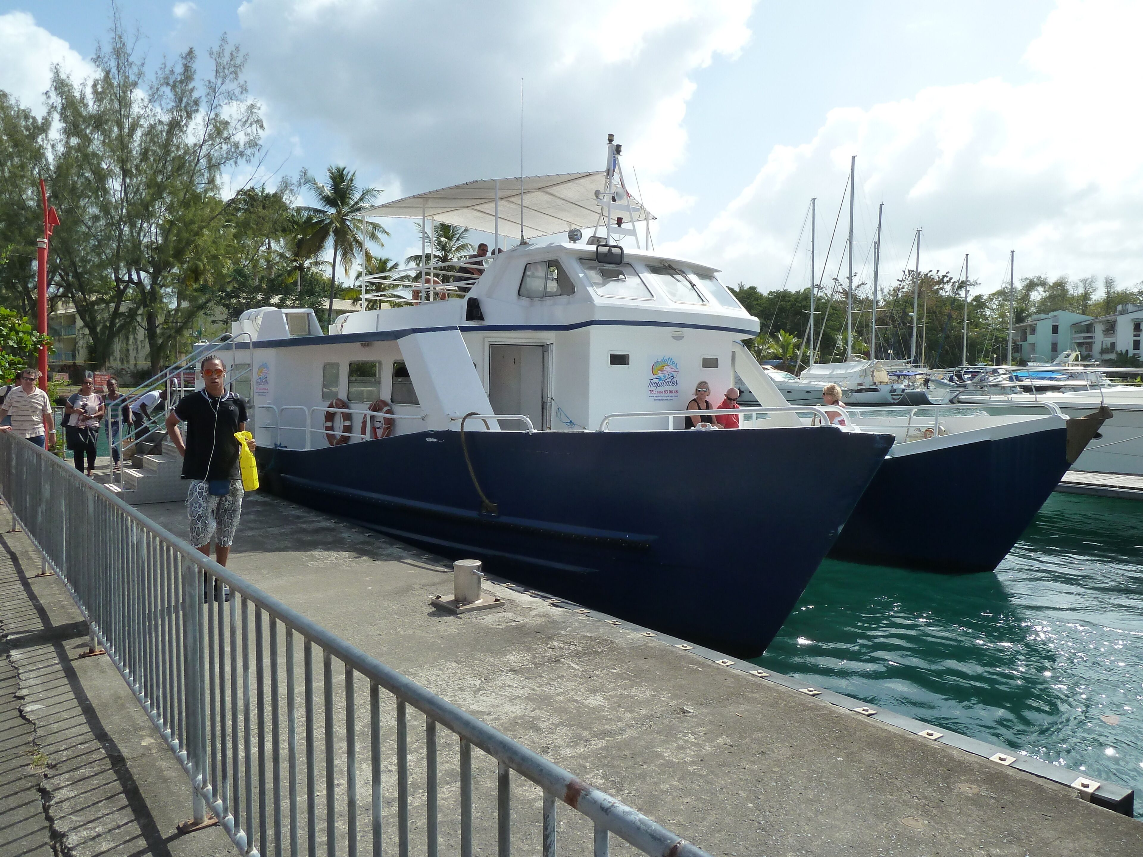 A large boat docked at a marina with a covered walkway and people walking nearby.