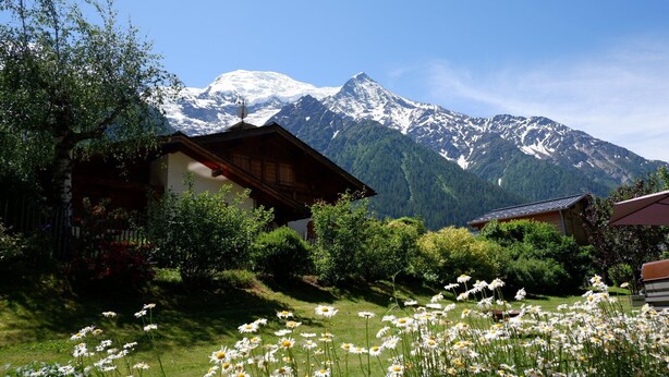Una cabaña de montaña con jardín delantero, rodeada de montañas nevadas.