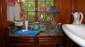 Un baño con tocador de madera, ventana con vistas a follaje, lavabo y una lámpara decorativa.