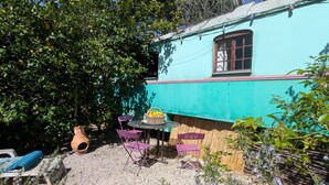 Un espacio de descanso al aire libre de estilo rústico, con una mesa, sillas, una cesta de mimbre y una planta en maceta.